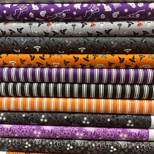 May include: A pile of Halloween-themed fabric rolls. The patterns feature skeletons, witch hats, ghosts, and stripes in black, orange, purple, and grey. The fabric is likely cotton or a similar material, suitable for crafting projects.