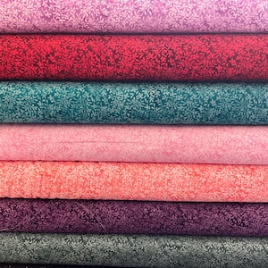 Puede incluir: Una pila de siete rollos de tela, cada uno con un patrón repetitivo de enredaderas y hojas en tonos similares. Los colores incluyen morado claro, rojo oscuro, verde azulado, rosa claro, coral, morado oscuro y gris carbón, dispuestos horizontalmente.