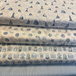 May include: Several rolls of fabric with seaside patterns. The top roll has navy blue sailboats and lighthouses on a white background. Below, a roll with seashells and starfish. The bottom rolls show beach huts and blue and white stripes.