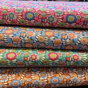 Könnte beinhalten: Ein Stapel Stoffe mit floralen Mustern in verschiedenen Farben. Die oberste Schicht ist rosa mit blauen und grünen Blumen. Darunter befindet sich ein marineblauer Stoff mit orangefarbenen und gelben Blumen. Die unteren Schichten sind grün und braun.
