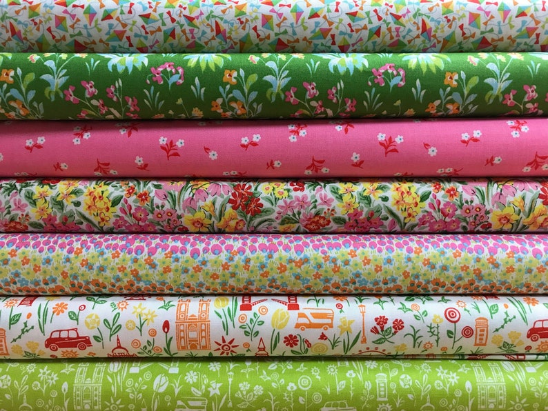 May include: A stack of six fabric rolls with various floral and city-themed patterns. The patterns include green leaves and pink flowers, yellow flowers, pink and blue flowers, a white background with red buses and buildings, and a green background with white buildings and buses.