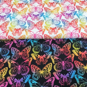 Puede incluir: Dos muestras de tela con un patrón repetitivo de mariposas de colores. La muestra superior es blanca con mariposas arcoíris. La muestra inferior es negra con mariposas arcoíris.