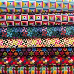 Puede incluir: Una pila de rollos de tela colorida con patrones geométricos. Los patrones incluyen cuadrados, triángulos y hexágonos en varios colores como azul, rosa, verde y amarillo. La tela parece ser de algodón o un material similar.