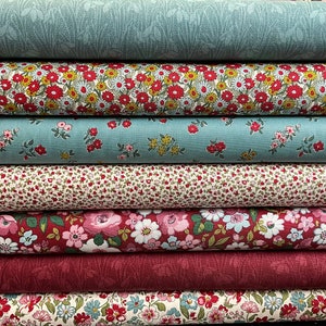 Könnte beinhalten: Ein Stapel von sechs Stoffrollen mit verschiedenen Blumenmustern. Die Rollen sind in Rot-, Weiß- und Blautönen gehalten. Der Stoff ist perfekt zum Quilten, Nähen und Basteln.