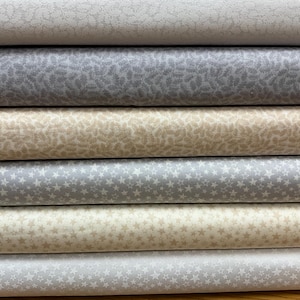 以下が含まれることがあります： グレーとベージュの様々な色合いのファブリック見本が5枚重ねられています。ファブリックには、小さな星や葉のデザインなど、さまざまなパターンが施されています。