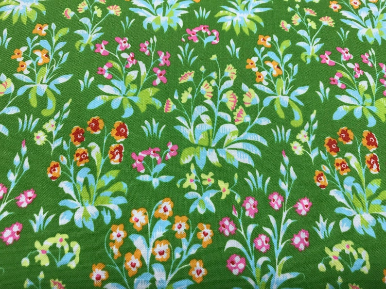 May include: Green fabric with a repeating pattern of small white, pink, orange, and yellow flowers. The flowers are arranged in clusters and are surrounded by green leaves.