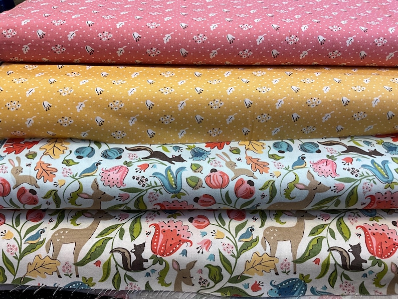 May include: Four rolls of fabric with various patterns. The top two rolls have small white floral and cloud patterns on pink and yellow backgrounds. The bottom two rolls feature woodland animal and floral designs on light blue and white backgrounds.