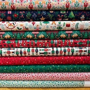 May include: A stack of ten bolts of fabric featuring various Christmas-themed patterns including nutcrackers, stars, bells, musical notes, and holiday ornaments in red, green, white, and navy blue colours, each wrapped around a white cardboard core.