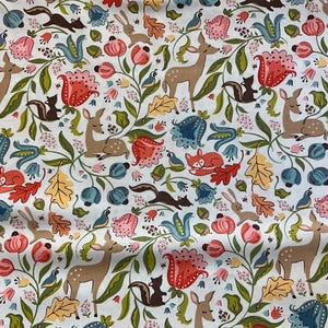 May include: A white fabric with a repeating pattern of woodland creatures and floral elements. The design includes deer, foxes, squirrels, rabbits, and birds, along with flowers and leaves in shades of red, blue, and green.