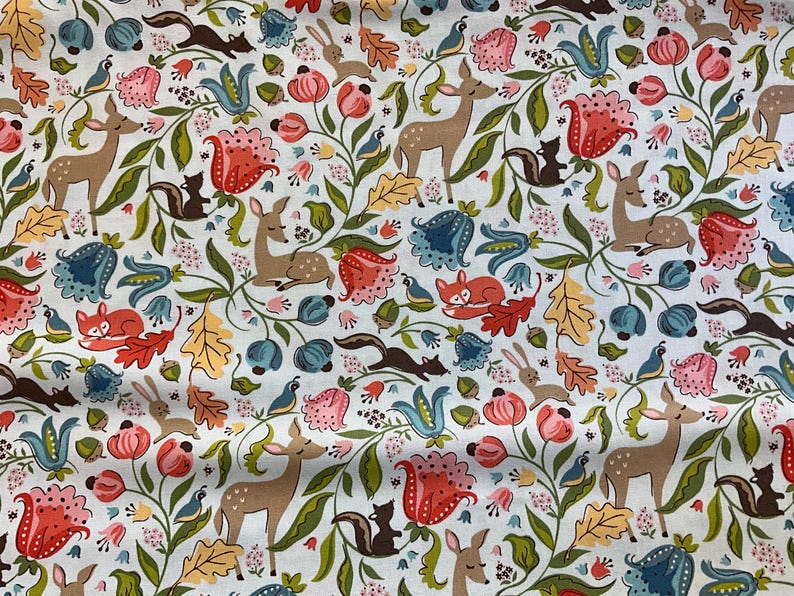 May include: A white fabric with a repeating pattern of woodland creatures and floral elements. The design includes deer, foxes, squirrels, rabbits, and birds, along with flowers and leaves in shades of red, blue, and green.