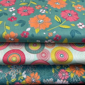 May include: Three fabric swatches with floral and geometric patterns. The top swatch is teal green with orange and pink flowers. The middle swatch is light green with pink and yellow concentric circles. The bottom swatch is teal green with orange and pink flowers.