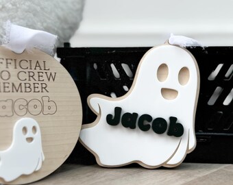 May include: Two wooden ghost ornaments with the name Jacob on them. One is a round ornament with the text "Official Boo Crew Member" and a small ghost image. The other is a ghost shaped ornament with a larger ghost image.