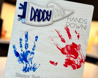 May include: A wooden sign with blue and red handprints, a blue banner with the text "Best Daddy Ever", and the text "Hands Down!"  Happy Father's Day 2024 Love Jacob & Edie