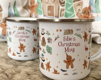 Puede incluir: Dos tazas de esmalte blanco con diseños navideños personalizados. Las tazas presentan casas de jengibre, estrellas y hombres de jengibre. Una taza dice "Jacob's Christmas Mug" y la otra dice "Edie's Christmas Mug".