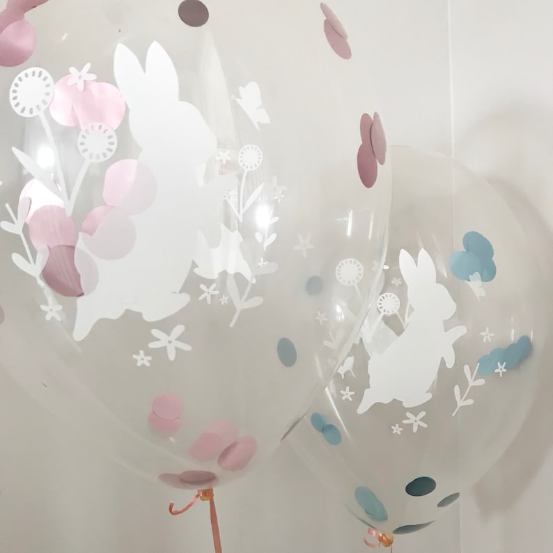 May include: Two clear balloons with white bunny silhouettes and confetti. The balloon on the left has pink confetti and the balloon on the right has blue confetti.