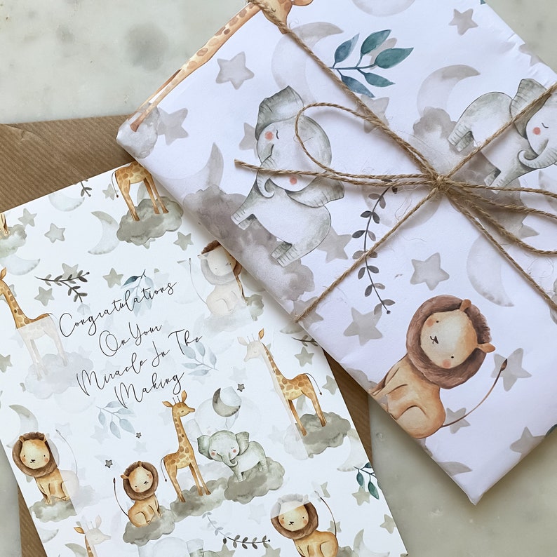 May include: A white card with a watercolor design of giraffes, lions, and elephants on clouds. The card says "Congratulations on your miracle in the making". The card is wrapped in white wrapping paper with a watercolor design of giraffes, lions, and elephants on clouds. The wrapping paper is tied with twine.