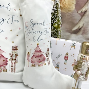 May include: White Christmas stocking with a pink and gold nutcracker theme. The stocking has the text "Special Delivery For Edie" printed on it.