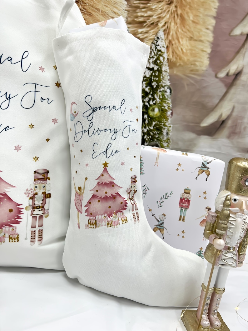 May include: White Christmas stocking with a pink and gold nutcracker theme. The stocking has the text "Special Delivery For Edie" printed on it.