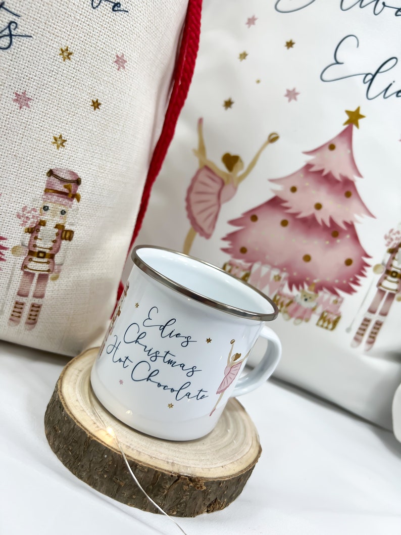 May include: White enamel mug with a pink ballerina and gold stars. The mug says "Edie's Christmas Hot Chocolate".