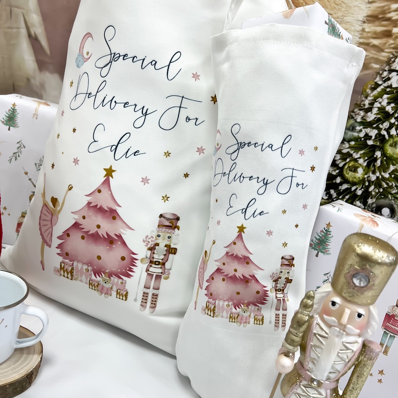 May include: Two white canvas stockings with pink and gold Christmas tree designs and the text "Special Delivery For Edie". A nutcracker figurine is in the foreground.