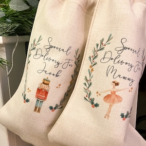 Pode incluir: Duas meias de Natal bege com um design festivo. Uma meia apresenta um quebra-nozes e o texto "Special Delivery For Jacob". A outra meia apresenta uma bailarina e o texto "Special Delivery For Mammy".