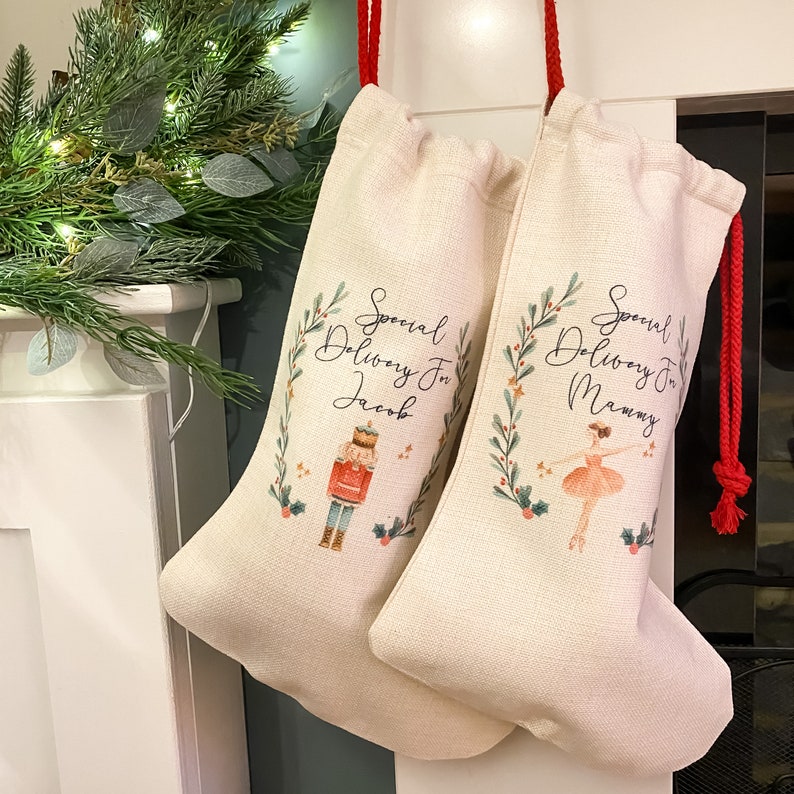 Pode incluir: Duas meias de Natal bege com cord&otilde;es de aperto vermelhos. A meia &agrave; esquerda tem uma ilustra&ccedil;&atilde;o de Quebra-Nozes e o texto "Special Delivery For Jacob". A meia &agrave; direita tem uma ilustra&ccedil;&atilde;o de bailarina e o texto "Special Delivery For Mommy".