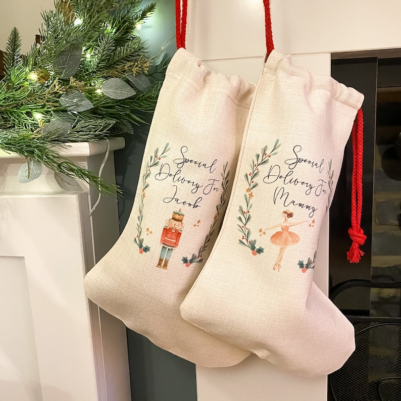 Pode incluir: Duas meias de Natal bege com cord&otilde;es de ajuste vermelhos. A meia da esquerda tem uma ilustra&ccedil;&atilde;o de quebra-nozes e o texto "Special Delivery For Jacob". A meia da direita tem uma ilustra&ccedil;&atilde;o de bailarina e o texto "Special Delivery For Mommy".