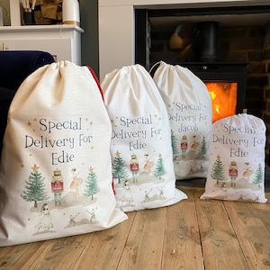 May include: Four white fabric gift bags featuring a Nutcracker and ballerina design. The bags are personalised with the names "Edie" and "Jacob". The text on the bags reads "Special Delivery For".