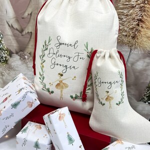 May include: Two personalized Christmas gift bags with red drawstrings. The larger bag has the text "Special Delivery For Georgia" and a ballerina illustration. The smaller bag has the text "Georgia" and a ballerina illustration. Both bags are made of natural linen fabric.