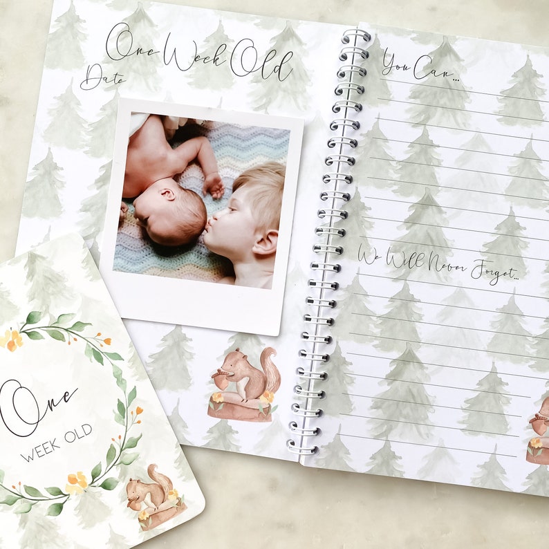 K&ouml;nnte beinhalten: Ein Baby-Erinnerungsbuch mit einem gr&uuml;nen und wei&szlig;en Aquarell-Baum-Muster. Der Einband zeigt ein Foto eines Babys und eines Kindes, die sich k&uuml;ssen. Der Text auf dem Einband lautet "One Week Old". Die Innenseite hat den Text "You Can... We Will Never Forget."