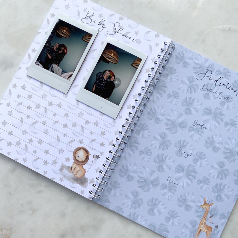 May include: A baby shower guest book with a blue and white cover featuring a giraffe and a lion. The inside pages have a star and moon pattern and a section for predictions about the baby's birth.