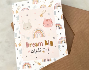 May include: A white card with a pink background and a rainbow pattern. The card has a pink bunny and a pink cat on it. The text on the card says "Dream Big. Little One."