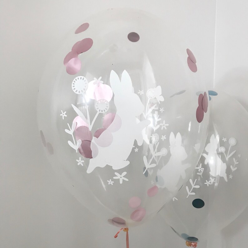 May include: Two clear balloons with white bunny and floral designs. The balloons are filled with pink and brown confetti.