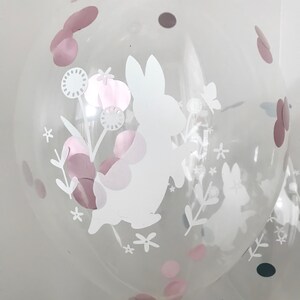 May include: Clear balloon with a white bunny rabbit and floral design. The balloon is decorated with pink and grey confetti.