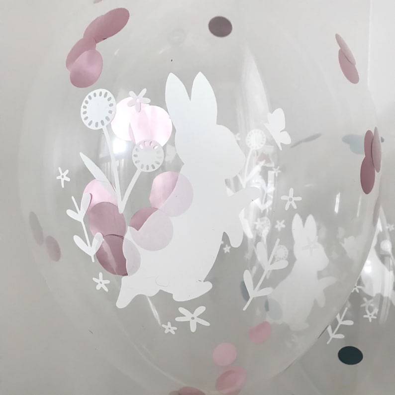 May include: Clear balloon with a white bunny rabbit and floral design. The balloon is decorated with pink and grey confetti.