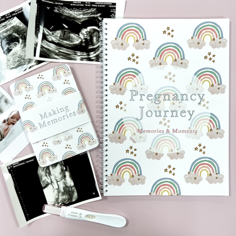 May include: A white pregnancy journal with a rainbow and cloud pattern. The cover reads "Pregnancy Journey Memories & Moments".
