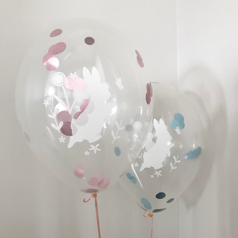 May include: Two clear balloons with white bunny silhouettes and confetti inside. The larger balloon has pink confetti and the smaller balloon has blue confetti.