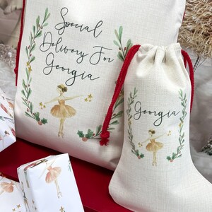 May include: A white canvas Christmas stocking with a red drawstring and a ballerina illustration. The stocking is personalized with the name "Georgia" and the text "Special Delivery For Georgia".