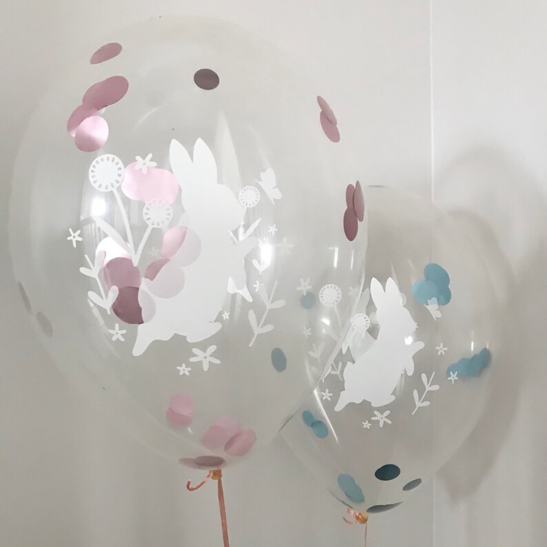 May include: Two clear balloons with white bunny silhouettes and confetti. The balloon on the left has pink confetti and the balloon on the right has blue confetti.