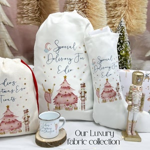 May include: A set of three white fabric gift bags with a pink and gold Christmas tree design. The bags feature a ballerina, a nutcracker, and the text "Special Delivery For Edie".