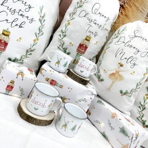 May include: White Christmas gift bags with personalized names, "Merry Christmas Caleb", "Quinn's Christmas Treats", and "Special Delivery for Molly". The bags are decorated with a nutcracker and ballerina illustrations. There are also four white enamel mugs with the names "Jacob" and a nutcracker and ballerina illustration.