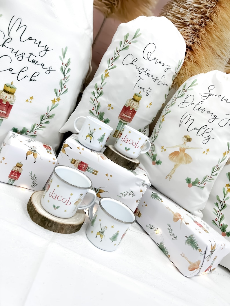 May include: White Christmas gift bags with personalized names, "Merry Christmas Caleb", "Quinn's Christmas Treats", and "Special Delivery for Molly". The bags are decorated with a nutcracker and ballerina illustrations. There are also four white enamel mugs with the names "Jacob" and a nutcracker and ballerina illustration.