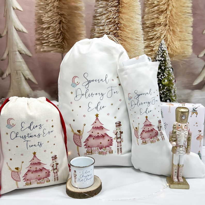May include: A set of four Christmas gift bags with a pink and gold ballerina and nutcracker theme. The bags are made of white fabric with red trim and feature the text "Special Delivery for Edie" and "Edie's Christmas Eve Treats".