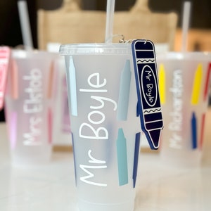 May include: A white reusable cup with a blue crayon design and the name "Mr. Boyle" written on it. The cup has a straw and a blue crayon keychain attached.