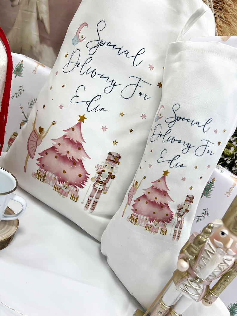 May include: Two white fabric stockings with pink and gold illustrations of a Christmas tree, a ballerina, and a nutcracker. The stockings have the text "Special Delivery For Edie" on them.