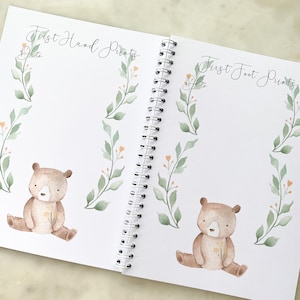 K&ouml;nnte beinhalten: Ein wei&szlig;es Buch mit einer Spiralbindung. Der Einband hat den Text "First Hand Prints" und "First Foot Prints" mit einer Aquarell-Illustration eines B&auml;ren und Bl&auml;ttern.