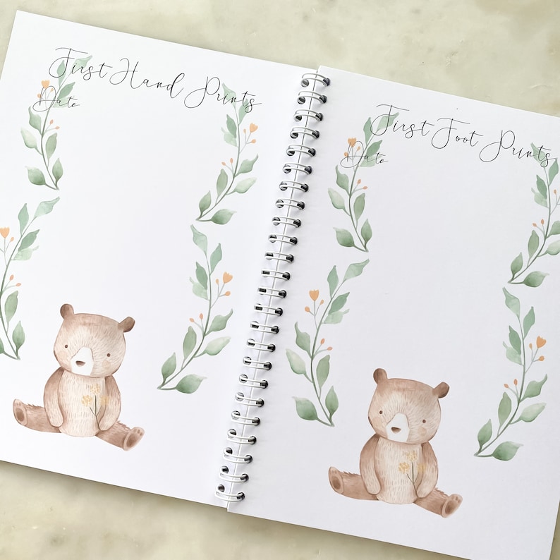 K&ouml;nnte beinhalten: Ein wei&szlig;es Buch mit einer Spiralbindung. Der Einband hat den Text "First Hand Prints" und "First Foot Prints" mit einer Aquarell-Illustration eines B&auml;ren und Bl&auml;ttern.