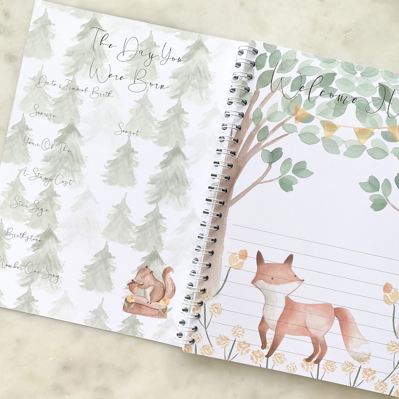 K&ouml;nnte beinhalten: Ein Baby-Erinnerungsbuch mit einer Aquarell-Illustration eines Fuchses in einer Waldlandschaft. Der Einband zeigt den Text "Willkommen Zuhause" mit einer Fahnenkette. Die Innenseite hat eine Aquarell-Illustration eines Eichh&ouml;rnchens in einer Waldlandschaft mit dem Text "Der Tag, an dem du geboren wurdest".