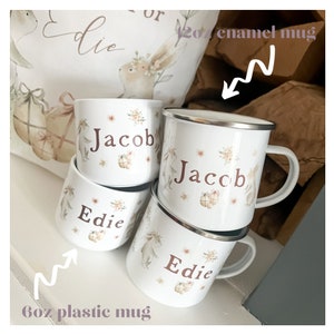 May include: Four personalized mugs, two white enamel mugs with the name "Jacob" and two white plastic mugs with the name "Edie". The mugs feature a brown bunny rabbit illustration with floral accents.