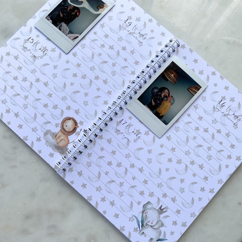 May include: A pregnancy journal with a white background and a pattern of stars and moons. The journal has a spiral binding and is open to pages 14, 15, 16, and 17. Each page has a space for a photo and a section for writing. The pages are decorated with illustrations of a lion, an elephant, and a baby.